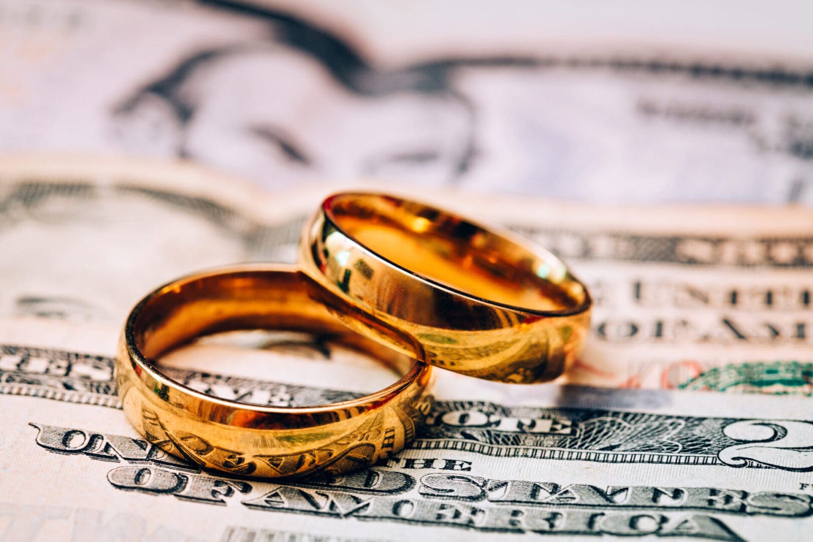 Two gold wedding rings sitting on top of a pile of money.