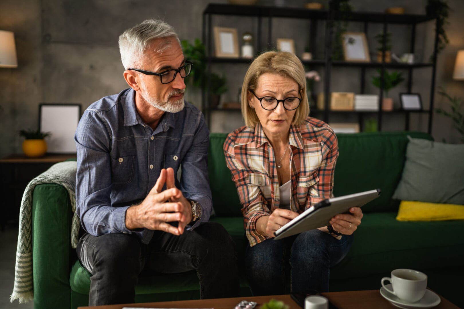 A man and woman sitting on the couch looking at an ipad.